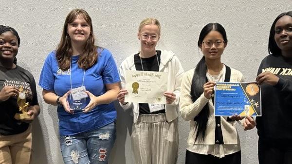 5 smiling students standing together holding awards and certificates